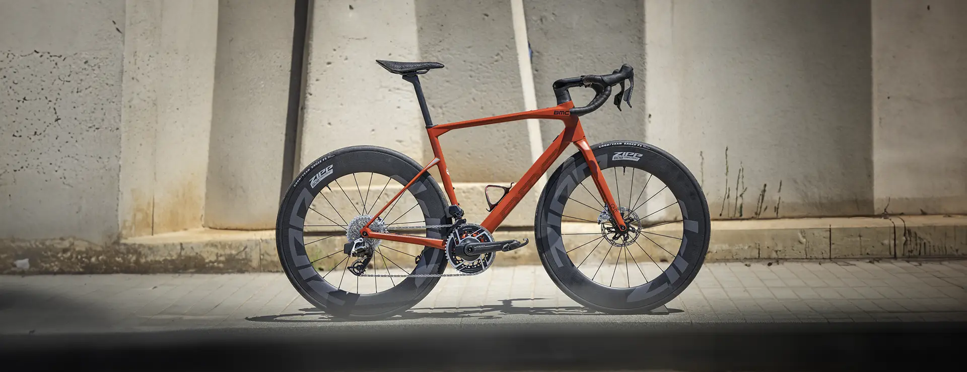 Una moderna bicicleta de carretera con cuadro rojo y ruedas de sección profunda, diseñada para el máximo rendimiento, se alza orgullosa contra una pared de hormigón.