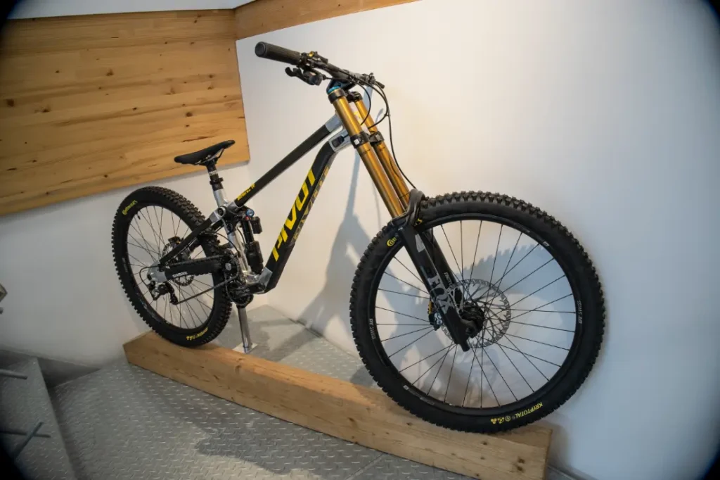 Una elegante bicicleta de montaña negra y amarilla de Central Europea de Pivot se encuentra orgullosamente montada en un soporte de madera contra la pared.