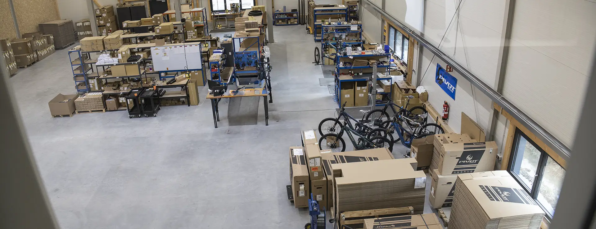 Vista aérea de la inauguración de un taller de montaje de bicicletas: diversos puestos de trabajo, piezas en cajas y bicicletas parcialmente montadas repartidas por el suelo de hormigón en previsión de convertirse en el nuevo pivote de operaciones de su sede central europea.