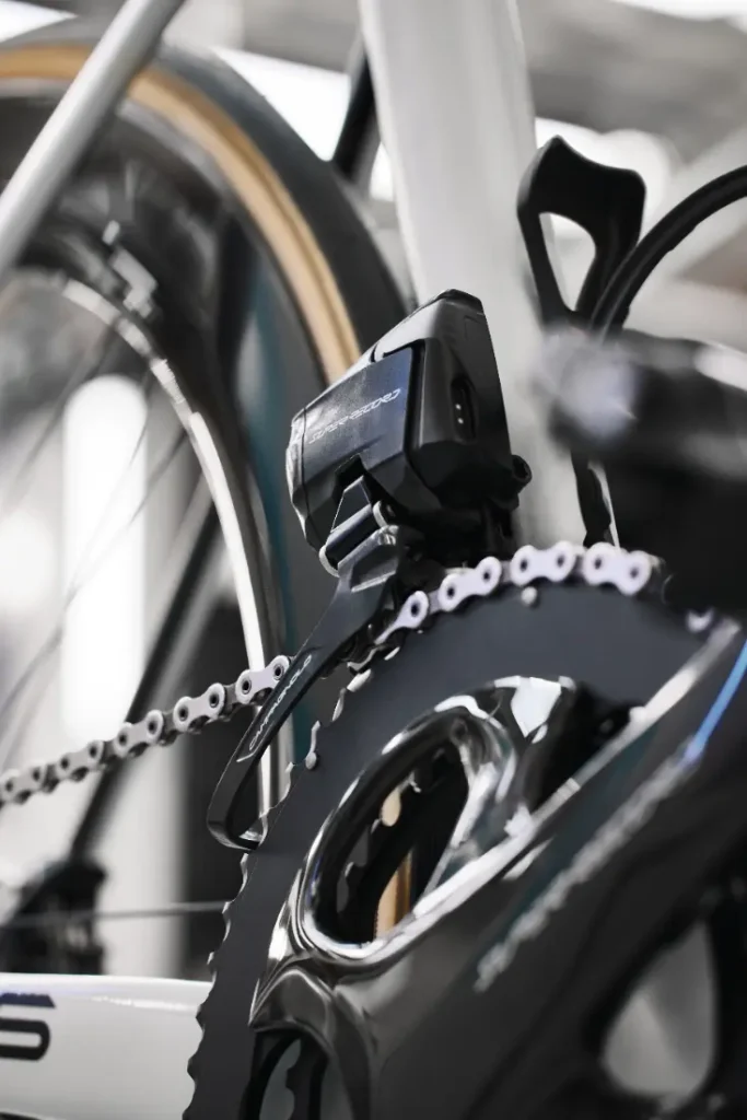 Primer plano de una cadena de bicicleta y un mecanismo de cambio, resaltando un dispositivo electrónico negro montado cerca del plato.