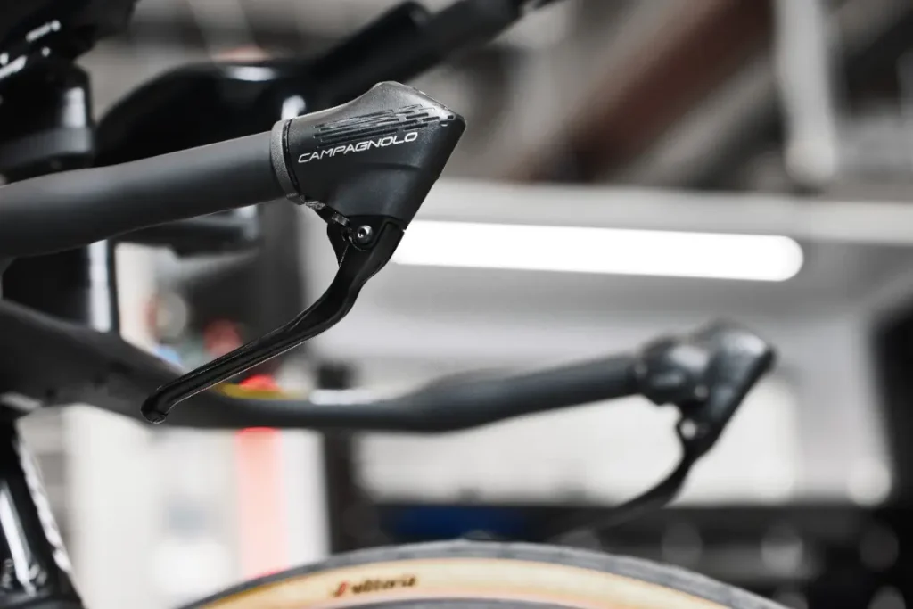 Primer plano de la palanca de cambios y el manillar de una bicicleta Campagnolo, con un fondo borroso.