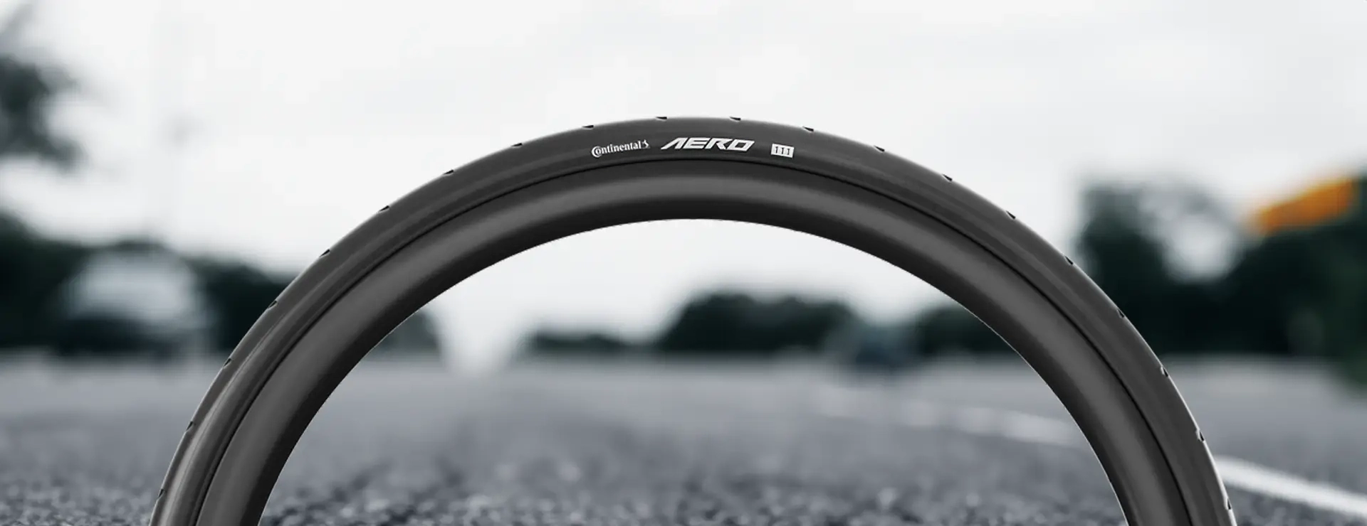 Primer plano de un neumático de bicicleta con la etiqueta "Aero 180", fabricado con una precisión similar a la del Continental AERO 111, sobre un fondo de carretera borrosa.