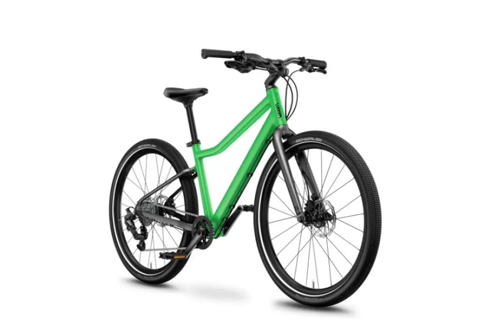 La bicicleta verde WOOM 4 Explore, con manubrio negro y un cuadro elegante, se destaca sobre el fondo blanco. Cuenta con frenos de disco y neumáticos anchos, diseñados para una conducción versátil.