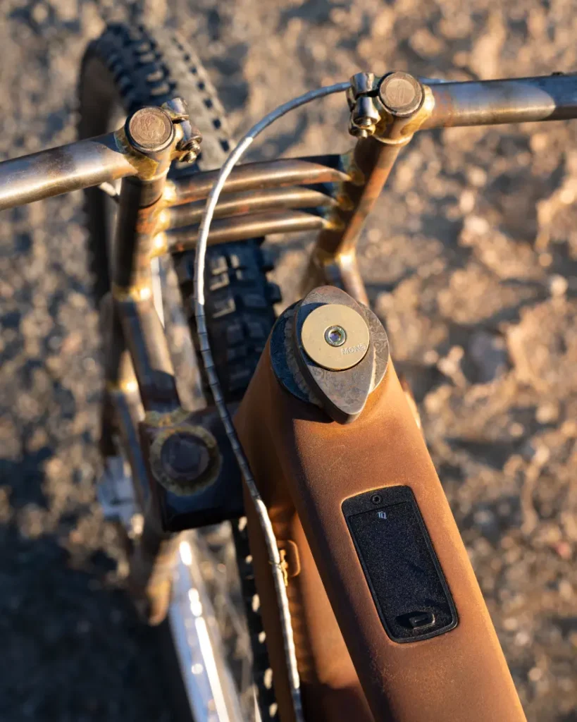 Primer plano de un cuadro de bicicleta SCOTT Solace oxidado con un candado de cable conectado al manillar y un soporte para teléfono inteligente montado en el vástago del manillar, frente a un camino de tierra baldío en el fondo.