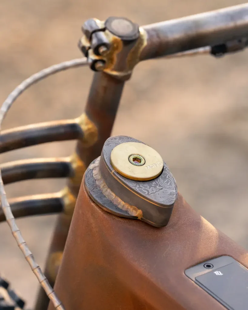 Primer plano de un manillar de bicicleta vintage SCOTT Solace y un cuadro oxidado, que presenta una pequeña tapa de metal decorativa con patrones intrincados y un acabado desgastado, que le da un evocador encanto de páramo.
