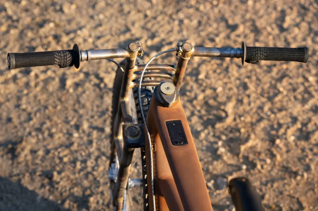 Vista de arriba hacia abajo de una bicicleta vintage con manillar oxidado y cuadro marrón, que recuerda a una SCOTT Solace explorando un terreno baldío con textura.