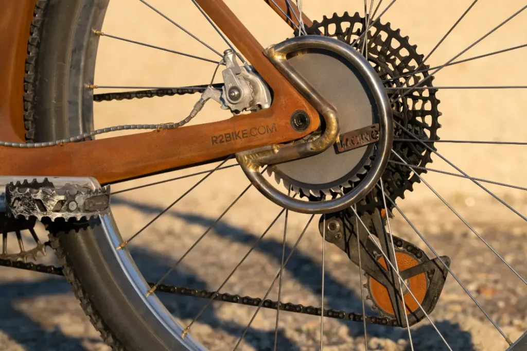 Primer plano de la rueda trasera y la transmisión de una bicicleta SCOTT Solace, con un cassette de cambios y un descarrilador parcialmente visible en el accidentado entorno de Wasteland.