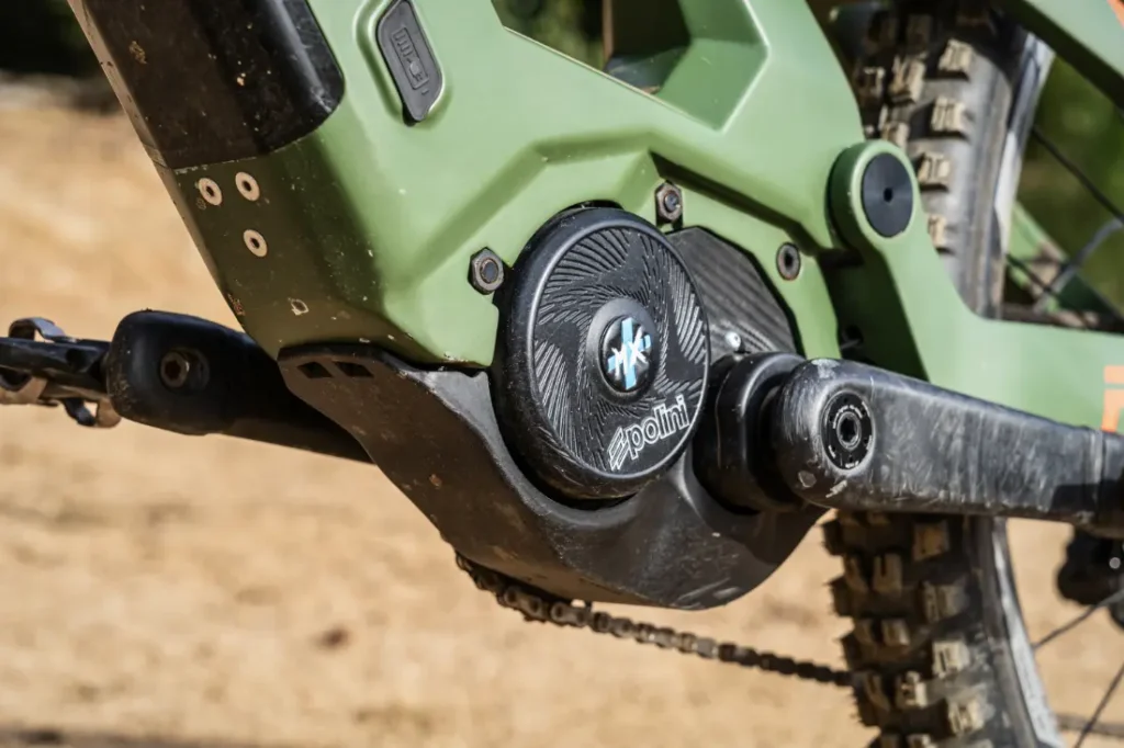 Primer plano del motor y el sistema de manivela Polini E-P3+ de una bicicleta de montaña eléctrica ecológica, que muestra componentes cubiertos de tierra y un neumático resistente, resaltando su potencia italiana en un entorno al aire libre.