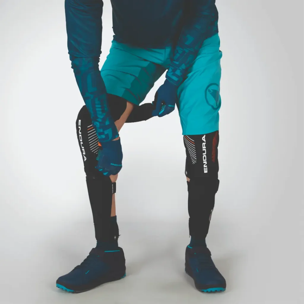 La persona vestida con ropa deportiva azul ajusta cuidadosamente sus rodilleras Endura, garantizando un ajuste seguro para una máxima protección.