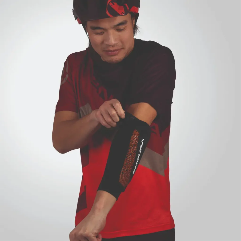 Una persona que viste un traje deportivo rojo y negro se ajusta la manga del brazo Endura.