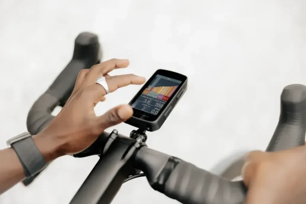 Una persona interactúa con un ciclocomputador montado en el manillar de una bicicleta, mostrando datos y gráficos en la pantalla.