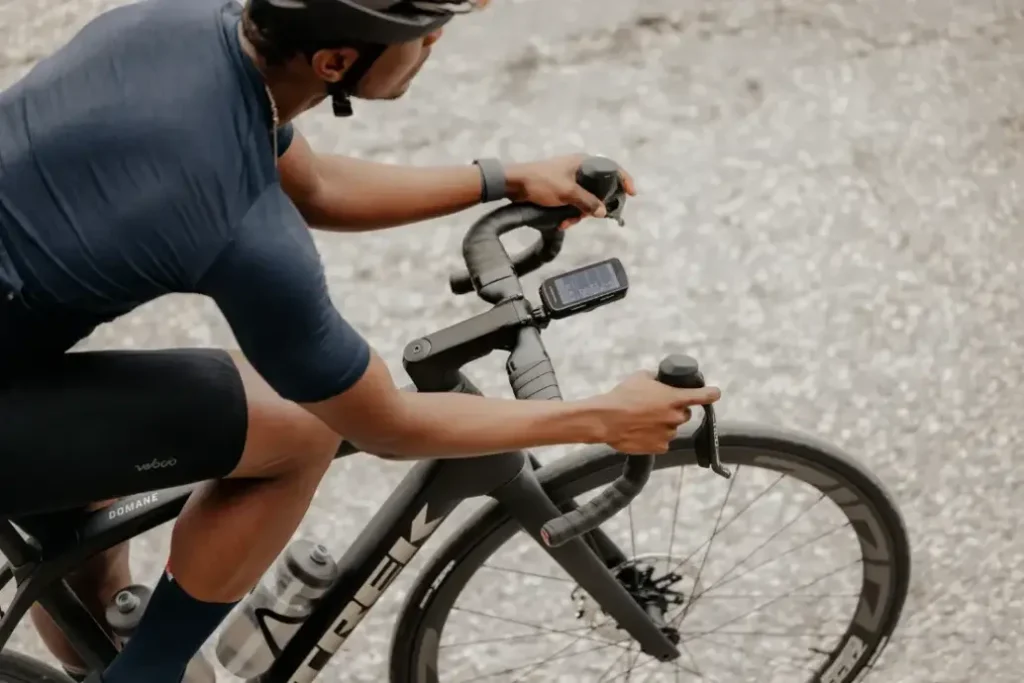 Un ciclista con casco y ropa azul conduce una bicicleta de carretera con un teléfono inteligente montado sobre una superficie de hormigón gris.