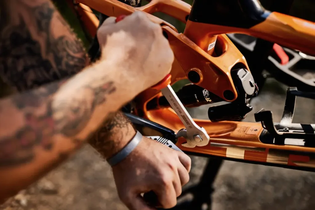 Una persona utiliza con destreza una llave Unior para ajustar el cuadro de una bicicleta de color naranja vibrante bajo el cielo abierto.