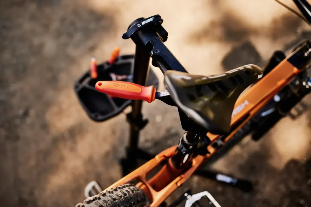 Una bicicleta de montaña en un soporte de reparación con herramientas Unior en una bandeja cercana está perfectamente posicionada en un camino de tierra.