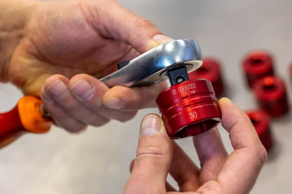Manos fijando con destreza un casquillo rojo Unior a una llave de trinquete, con otros casquillos rojos sutilmente visibles en el fondo.