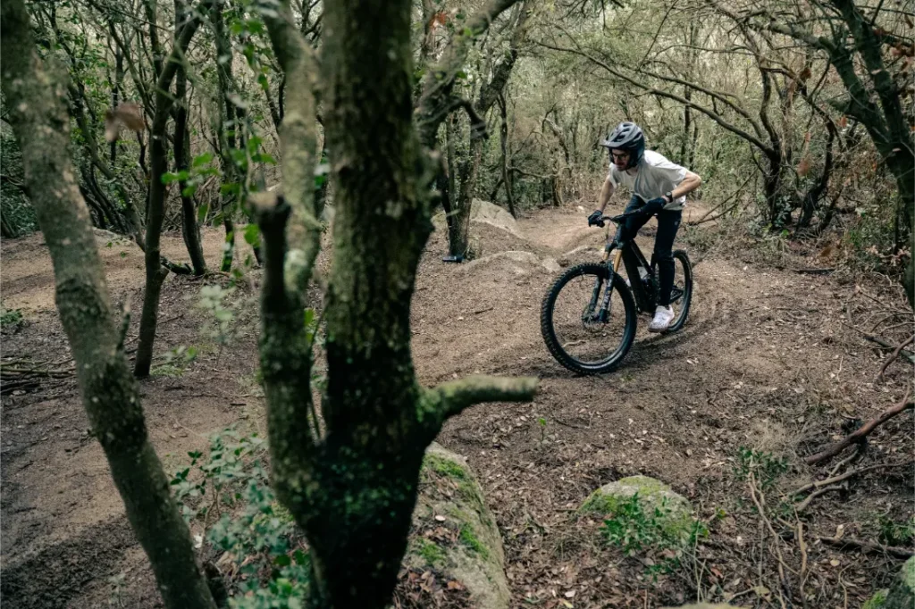 Una persona que lleva casco conduce una bicicleta de montaña UNNO MITH por un sendero de tierra accidentado que atraviesa un bosque denso.