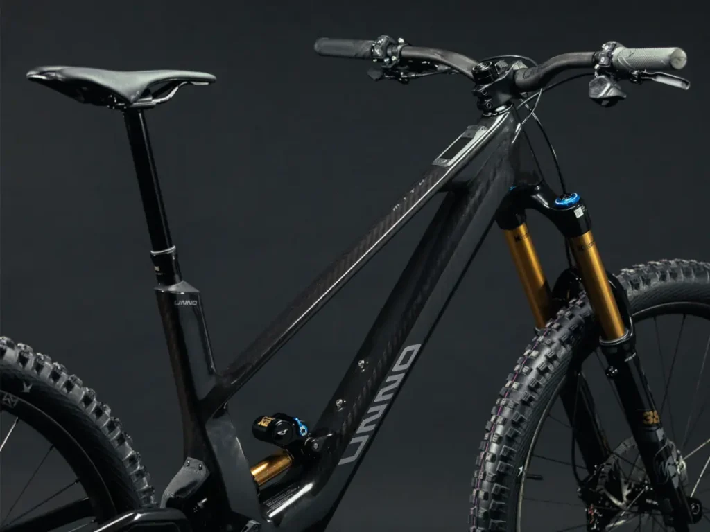 La UNNO MITH es una elegante bicicleta de montaña negra con un cuadro resistente, neumáticos con tacos y suspensión delantera, que se presenta perfectamente sobre un fondo oscuro y liso.