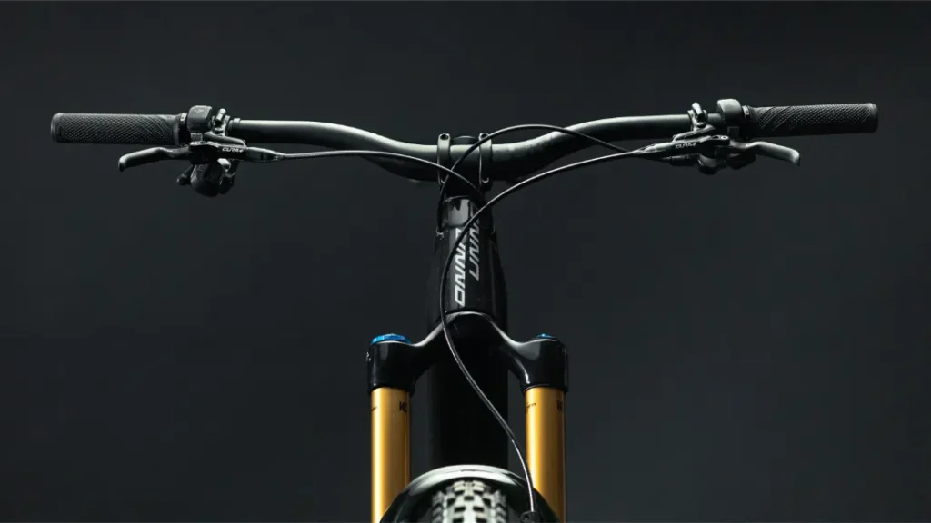Primer plano del manillar delantero y la horquilla de suspensión de una bicicleta UNNO MITH sobre un fondo oscuro. Esta elegante bicicleta parece lista para usar.