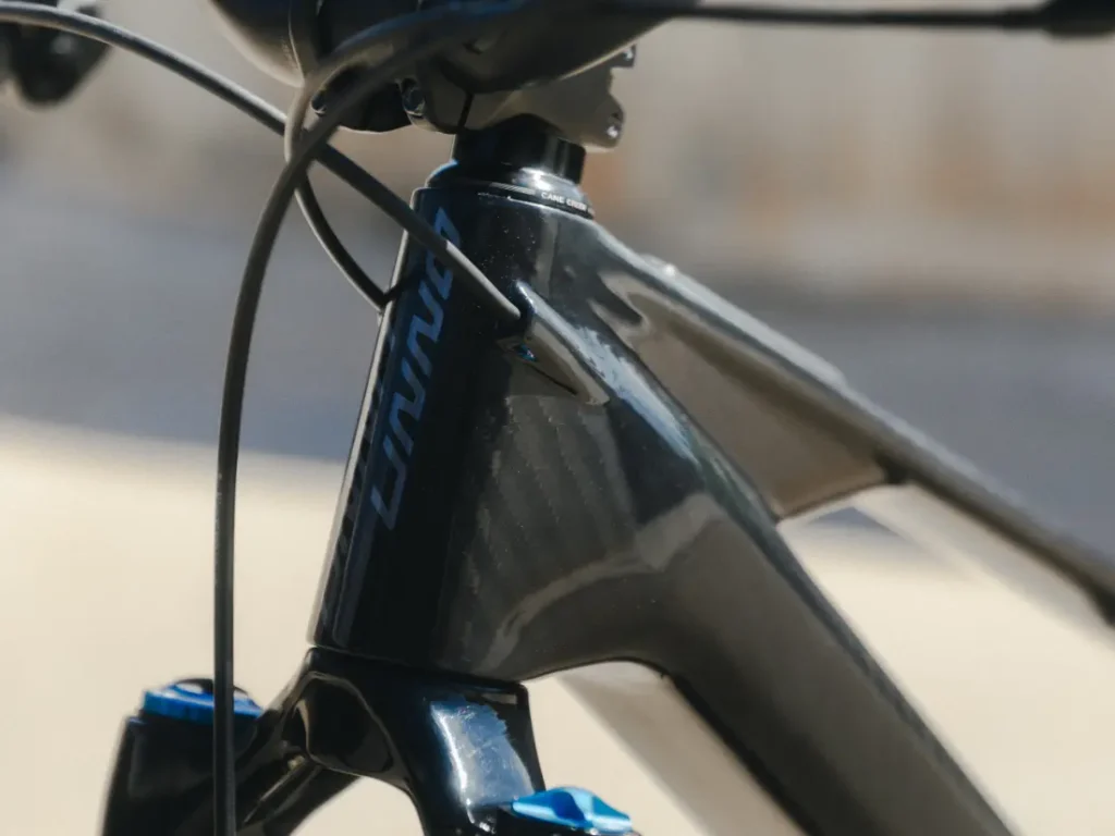 Primer plano del tubo de dirección y el manillar de una bicicleta negra, que muestra el logotipo UNNO MITH con detalles en azul y blanco en el cuadro.