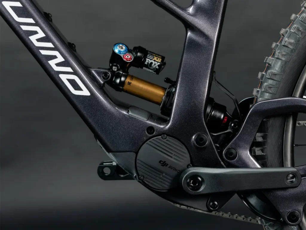Primer plano de un elegante cuadro de bicicleta eléctrica UNNO MITH negro con un sistema de suspensión FOX y un motor eléctrico integrado, con marca y cables visibles sobre un fondo oscuro.