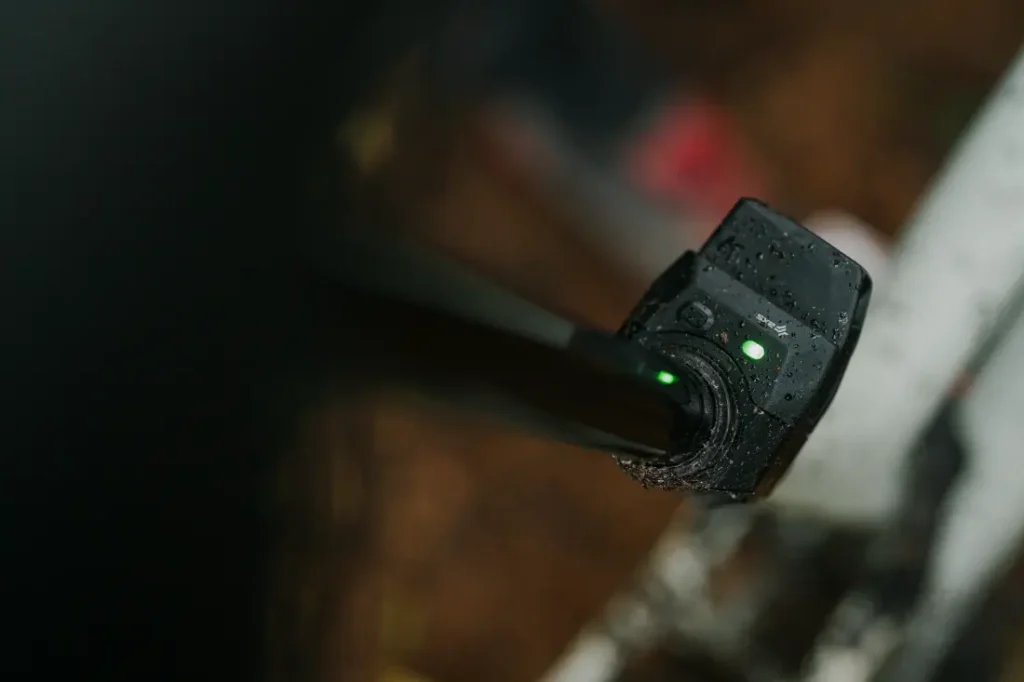 Primer plano de un cargador de bicicleta eléctrica húmedo conectado a una MTB, con una luz indicadora verde brillante.