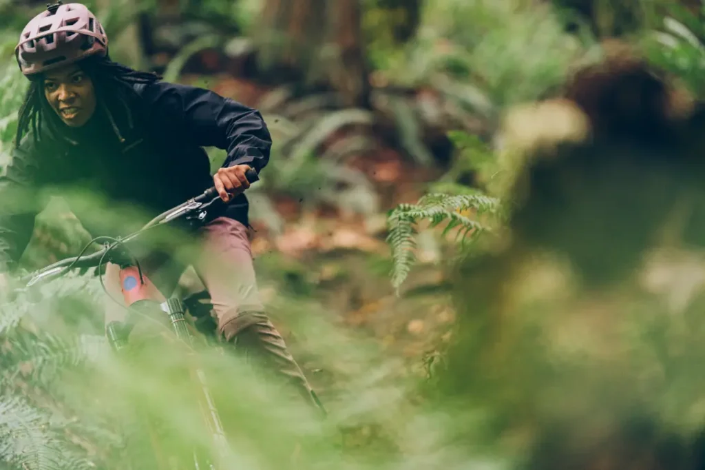 Una persona con casco recorre su MTB a través de una zona boscosa y exuberante, rodeada de vegetación, navegando sin esfuerzo por el terreno con la precisión de la tecnología RockShox Reverb AXS.