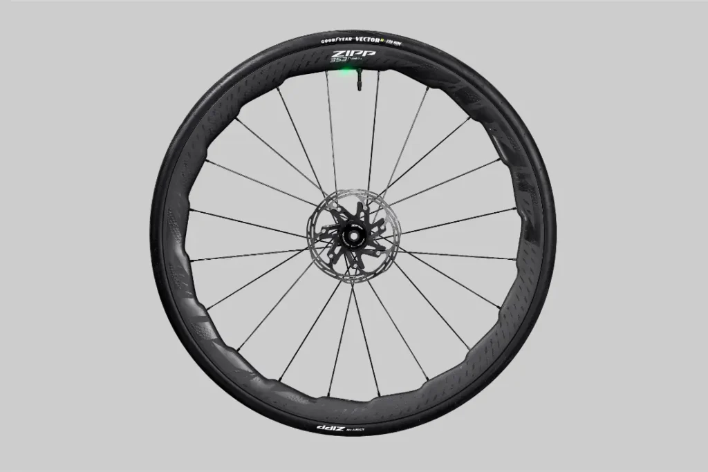 Una rueda de bicicleta Zipp 2026 de carbono negro con rotor de freno de disco y etiquetada "Zipp", diseñada para ayudarte a rodar más rápido, que se muestra sobre un fondo gris simple.