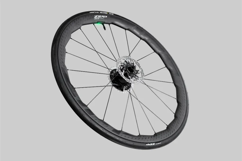 Se muestra una rueda de bicicleta Zipp 2026 negra con rotor de freno de disco, radios y neumático sin cámara sobre un fondo gris simple, diseñada para ayudarte a rodar más rápido en cada recorrido.