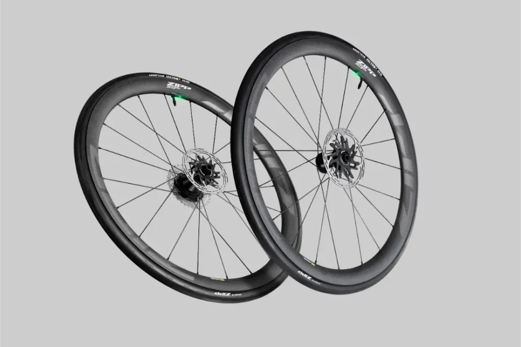 Un par de ruedas de bicicleta Zipp 2026 de fibra de carbono negra con frenos de disco, diseñadas para rodar más rápido, mostradas sobre un fondo gris liso.