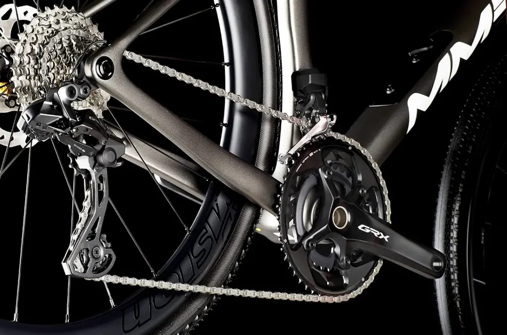 Primer plano de la transmisión de una bicicleta MMR Simun que muestra el desviador trasero, el cassette, la cadena y el juego de bielas GRX sobre un fondo negro.