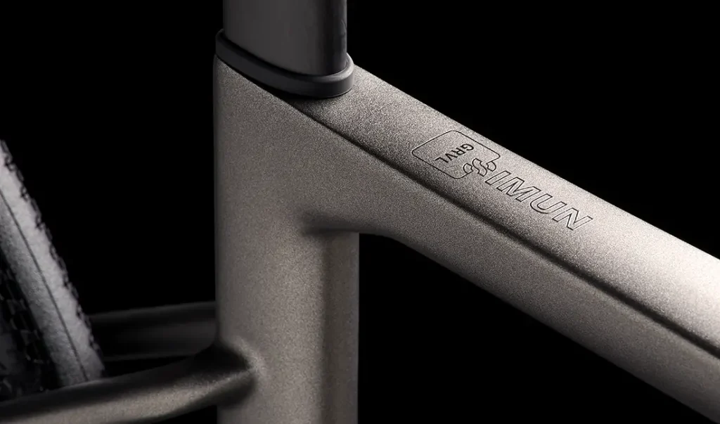 Primer plano de un cuadro de bicicleta MMR Simun gris mate que muestra la unión del tubo superior y el tubo del sillín, con el logotipo "IMUN" y "TMBR" grabado en el cuadro.