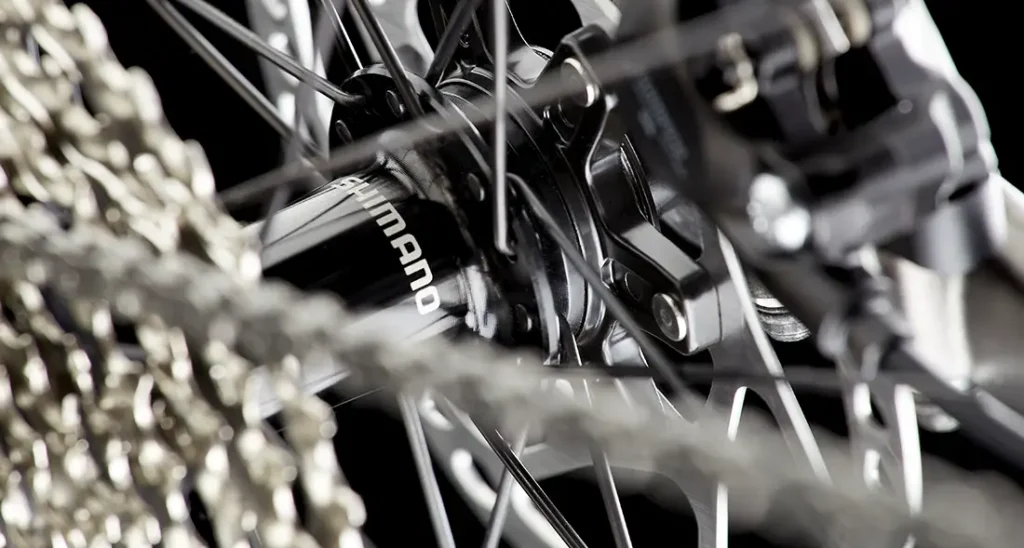 Primer plano de un buje de rueda trasera de bicicleta y un cassette de cambios con la marca "Shimano" visible y radios de metal, presentes en el modelo MMR Simun.