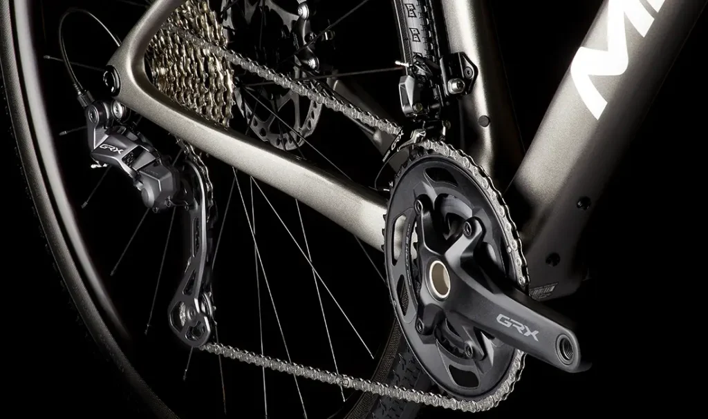 Primer plano de la transmisión de una bicicleta MMR Simun que muestra la cadena, el desviador trasero, el cassette y el juego de bielas delantero etiquetados "GRX" sobre un fondo oscuro.