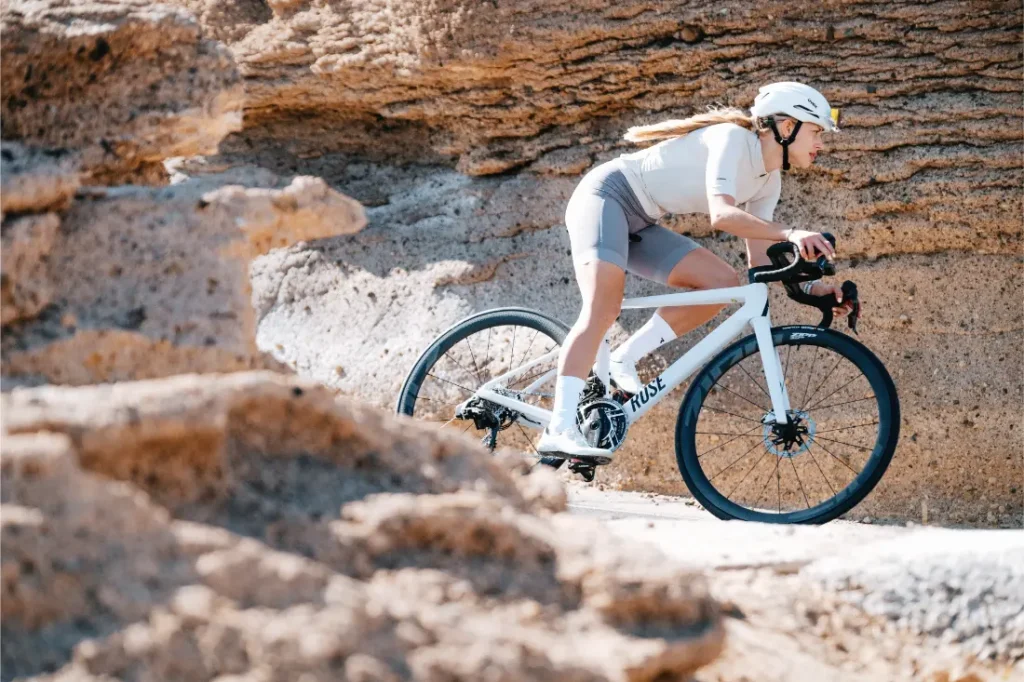 Un ciclista con casco y equipo de ciclismo conduce una bicicleta de carretera blanca con ruedas Zipp 2026 por un camino rocoso e iluminado por el sol, listo para rodar más rápido.
