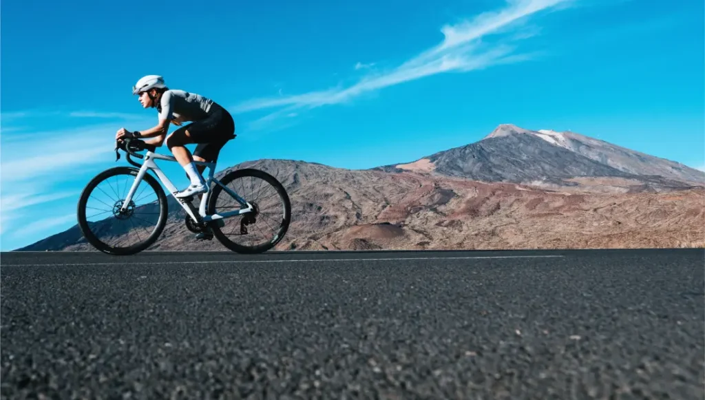 Un ciclista monta una bicicleta de carretera Zipp 2026 en una carretera pavimentada con un paisaje montañoso y un cielo azul, disfrutando de rodar más rápido en el pintoresco telón de fondo.