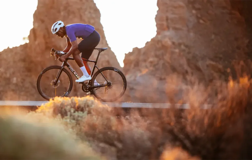 Un ciclista vestido con un maillot azul y un casco blanco circula con una bicicleta de carretera Zipp 2026 por un sendero al aire libre con formaciones rocosas al fondo, listo para rodar más rápido.