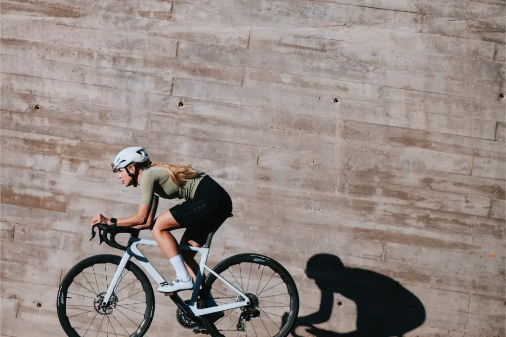 Una persona que lleva casco conduce una bicicleta de carretera con ruedas Zipp 2026 junto a una pared de hormigón texturizado, proyectando una sombra clara sobre la superficie.