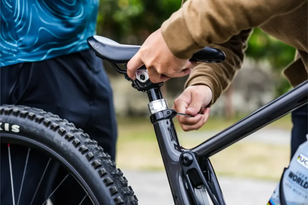 Una persona utiliza una llave Allen para ajustar la altura del sillín en una bicicleta negra equipada con una tija telescópica inalámbrica RAGE Circuit.