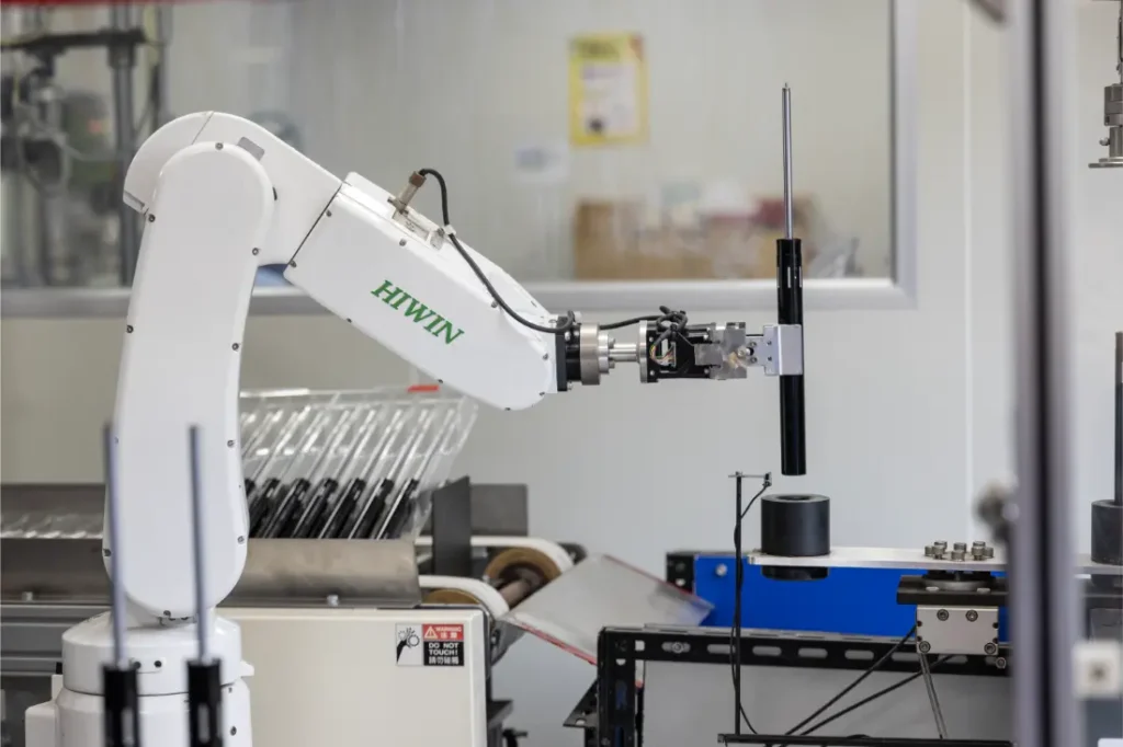 Un brazo robótico etiquetado como "HIWIN" opera en un laboratorio o en un entorno industrial, manipulando un objeto cilíndrico negro con un control preciso, similar a la manipulación de una tija telescópica inalámbrica.