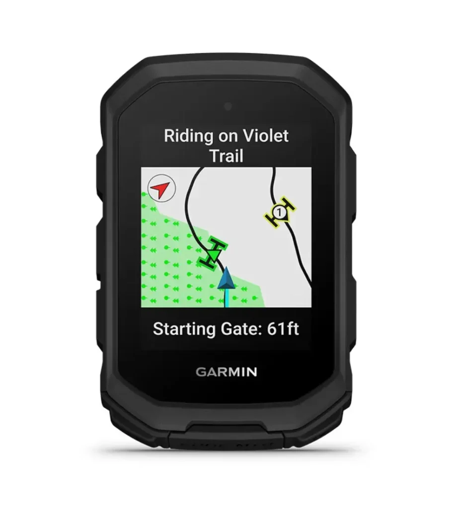 Un ciclocomputador Garmin Edge MTB muestra un mapa de senderos con el mensaje "Riding on Violet Trail" y "Starting Gate: 61 ft" en la pantalla.