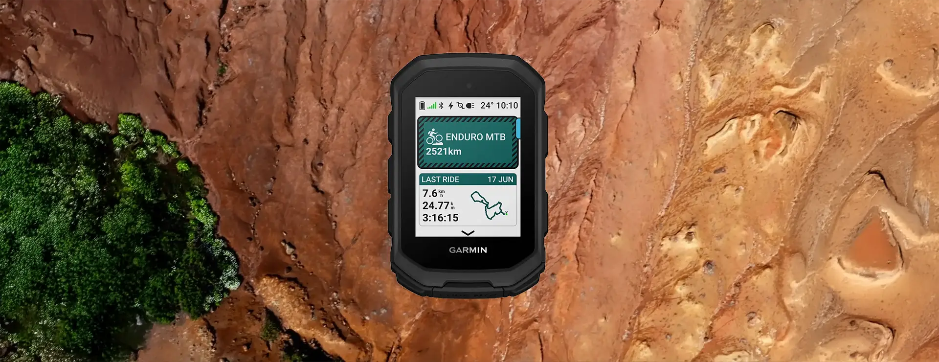 Un ciclocomputador Garmin Edge MTB que muestra la ruta, la distancia, la velocidad, la duración y la fecha destaca sobre un fondo de terreno rocoso rojizo y vegetación de un verde vibrante.
