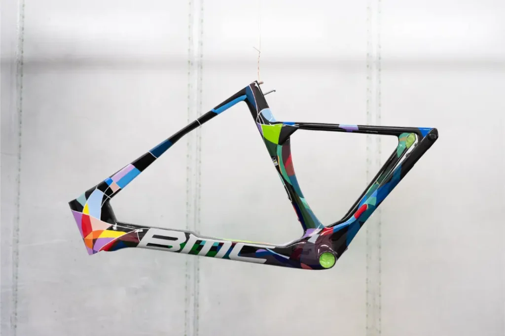 Un cuadro de bicicleta BMC VAR0 colorido con diseño geométrico y el logotipo de BMC cuelga suspendido sobre un fondo claro y liso.