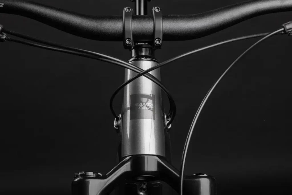Primer plano del manillar de aluminio, los cables y el tubo de dirección de una bicicleta Santa Cruz Vala AL con el logotipo de Santa Cruz, sobre un fondo negro.
