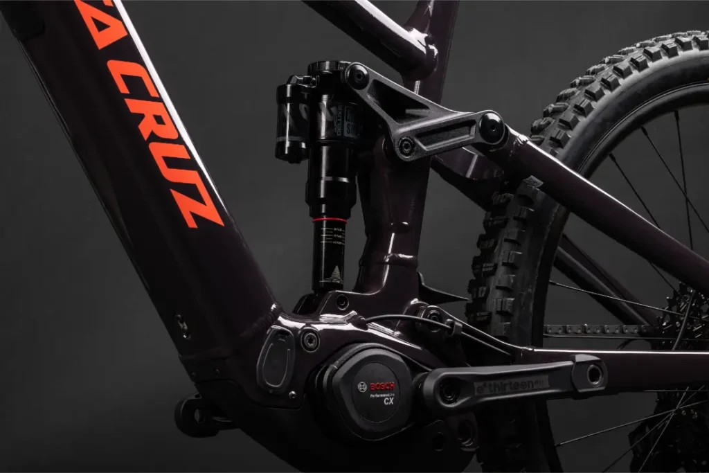 Primer plano de un cuadro de bicicleta de montaña Santa Cruz Vala AL en aluminio, destacando el motor Bosch CX, el varillaje de suspensión y la rueda trasera sobre un fondo oscuro.