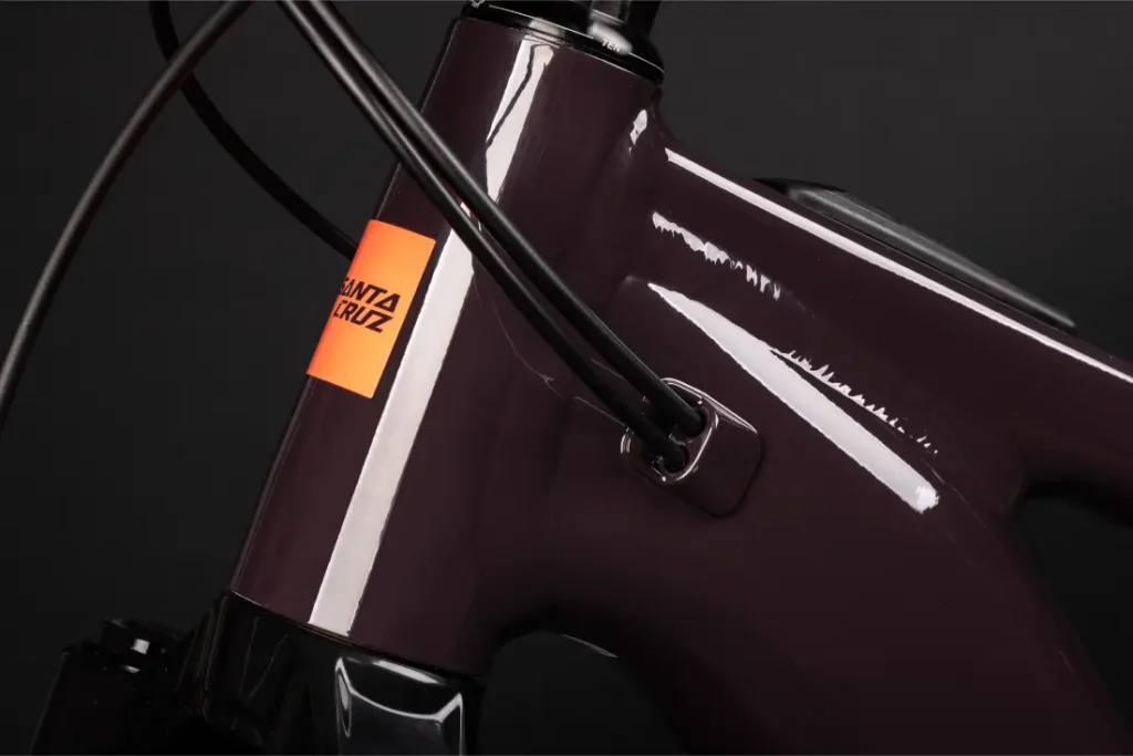 Primer plano de un cuadro de bicicleta Santa Cruz Vala AL aluminio de color púrpura oscuro que muestra el cableado interno y el logotipo de Santa Cruz de color naranja brillante sobre fondo negro.
