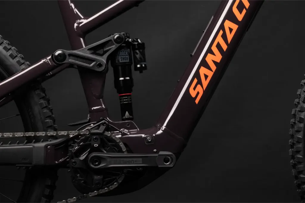 Primer plano de un cuadro de bicicleta de montaña Santa Cruz Vala AL en aluminio, mostrando la suspensión trasera, los platos y bielas, la cadena y parte de la rueda trasera sobre un fondo oscuro.