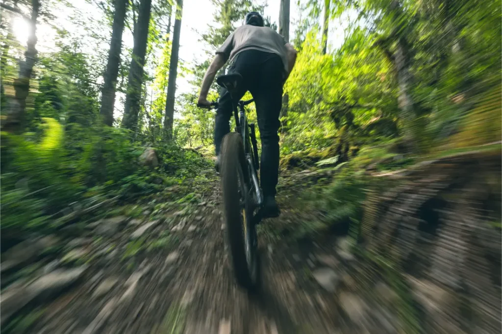 Una persona conduce una bicicleta de montaña Santa Cruz Vala AL por un sendero pedregoso de tierra a través de un bosque denso y verde. La imagen está difuminada para transmitir velocidad y destaca el ligero cuadro de aluminio de la bicicleta.