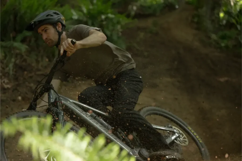 Una persona con casco conduce una bicicleta de montaña Santa Cruz Vala AL por un sendero de tierra, inclinándose en una curva mientras la suciedad y los escombros salen despedidos del robusto cuadro de aluminio.