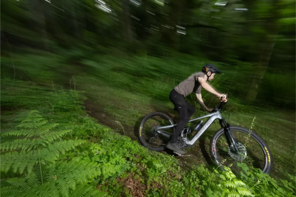 Una persona con casco monta en una bicicleta de montaña Santa Cruz Vala AL, fabricada en aluminio ligero, por un estrecho sendero en un frondoso y verde bosque.