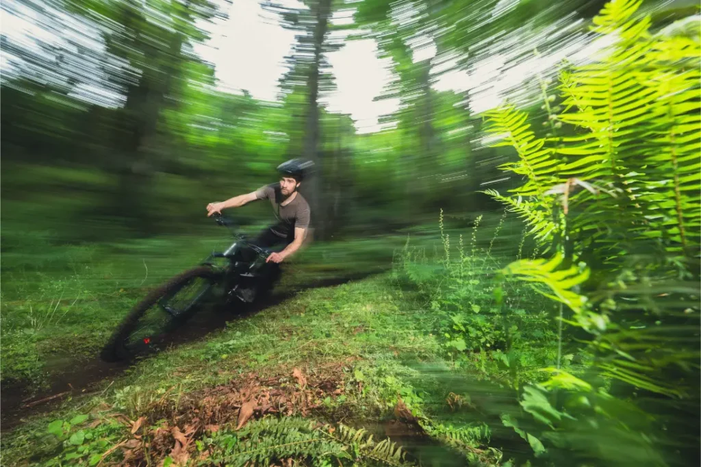 Una persona con casco monta en una bicicleta de montaña Santa Cruz Vala AL, cuyo ligero cuadro de aluminio se desliza rápidamente por un sendero forestal, con una vegetación borrosa que sugiere un rápido movimiento.